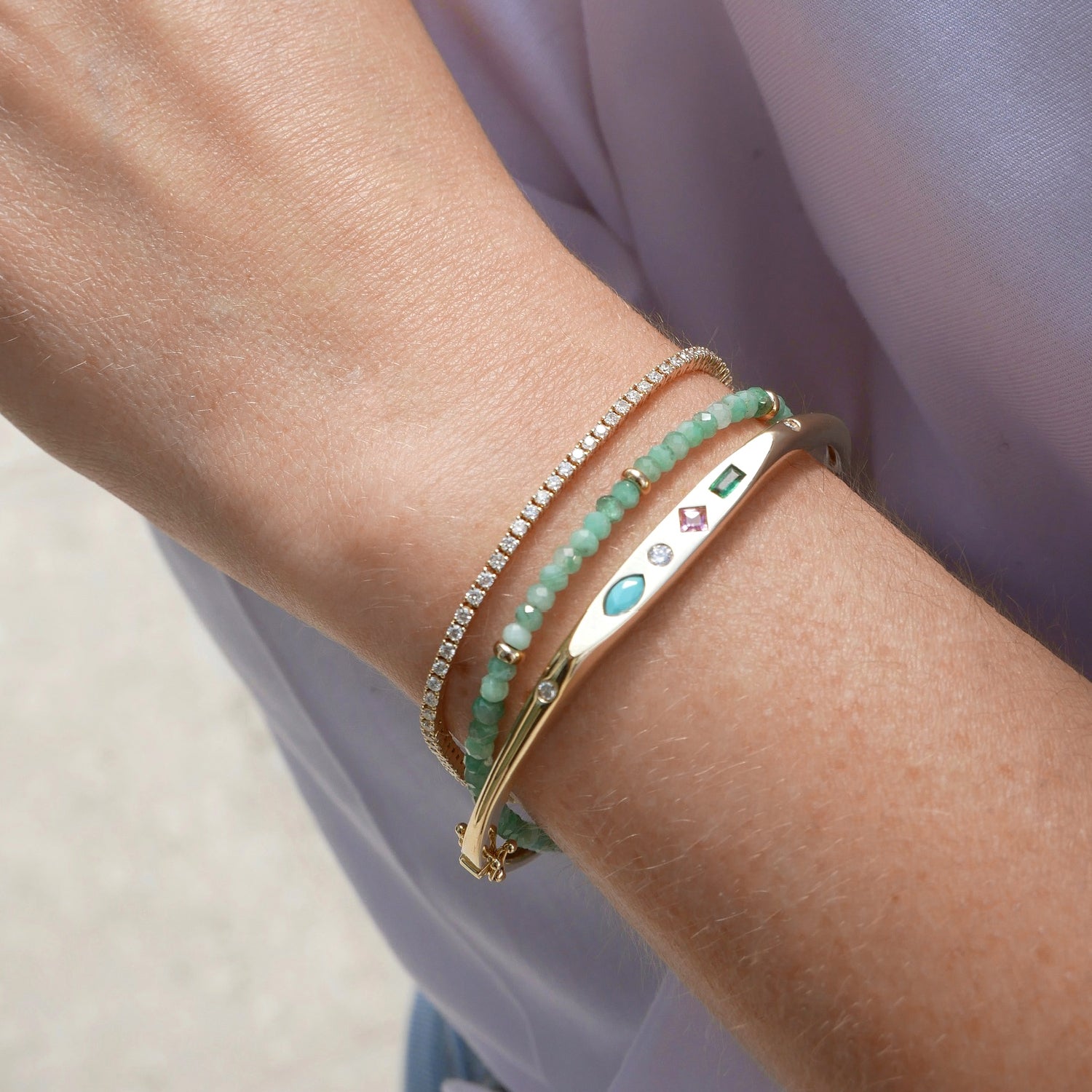 EF Collection 14k yellow gold treasure bangle styled on wrist of model next to aquamarine beaded bracelet and diamond grace bracelet