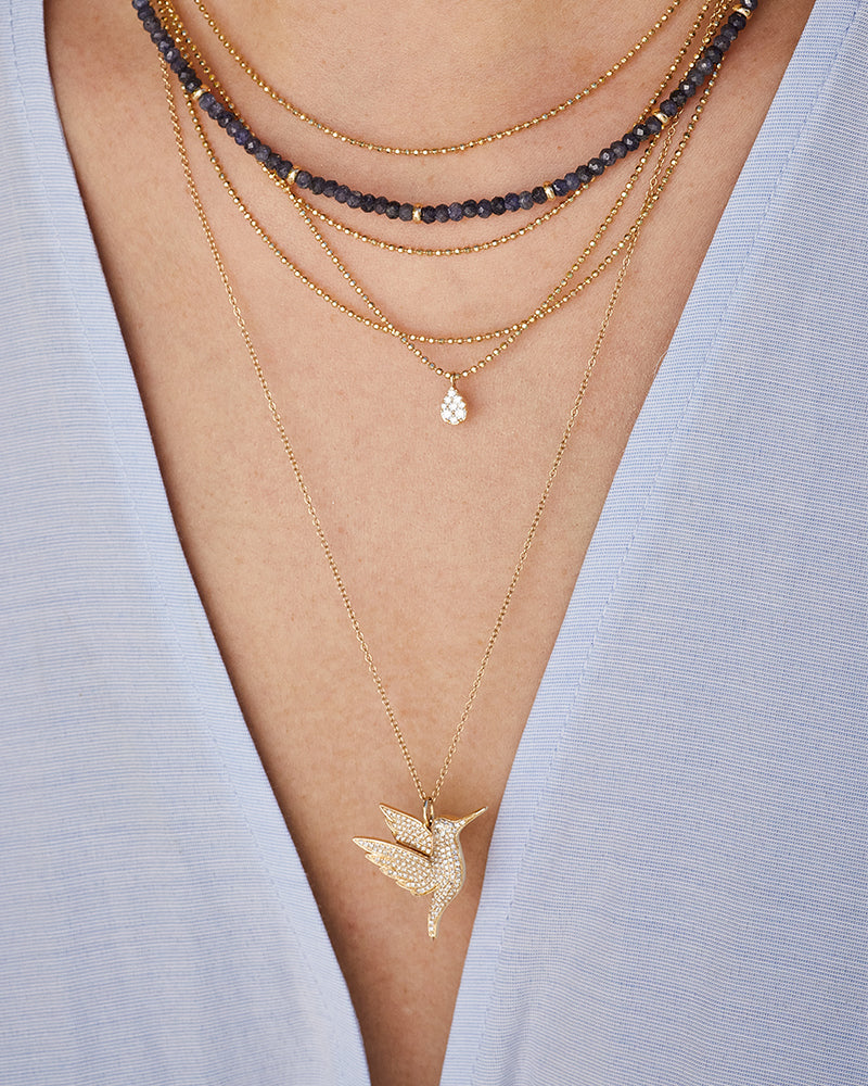 EF Collection 14k yellow gold layering necklaces styled on neck of model with hummingbird pendant, diamond teardrop pendant, and blue sapphire beaded necklace