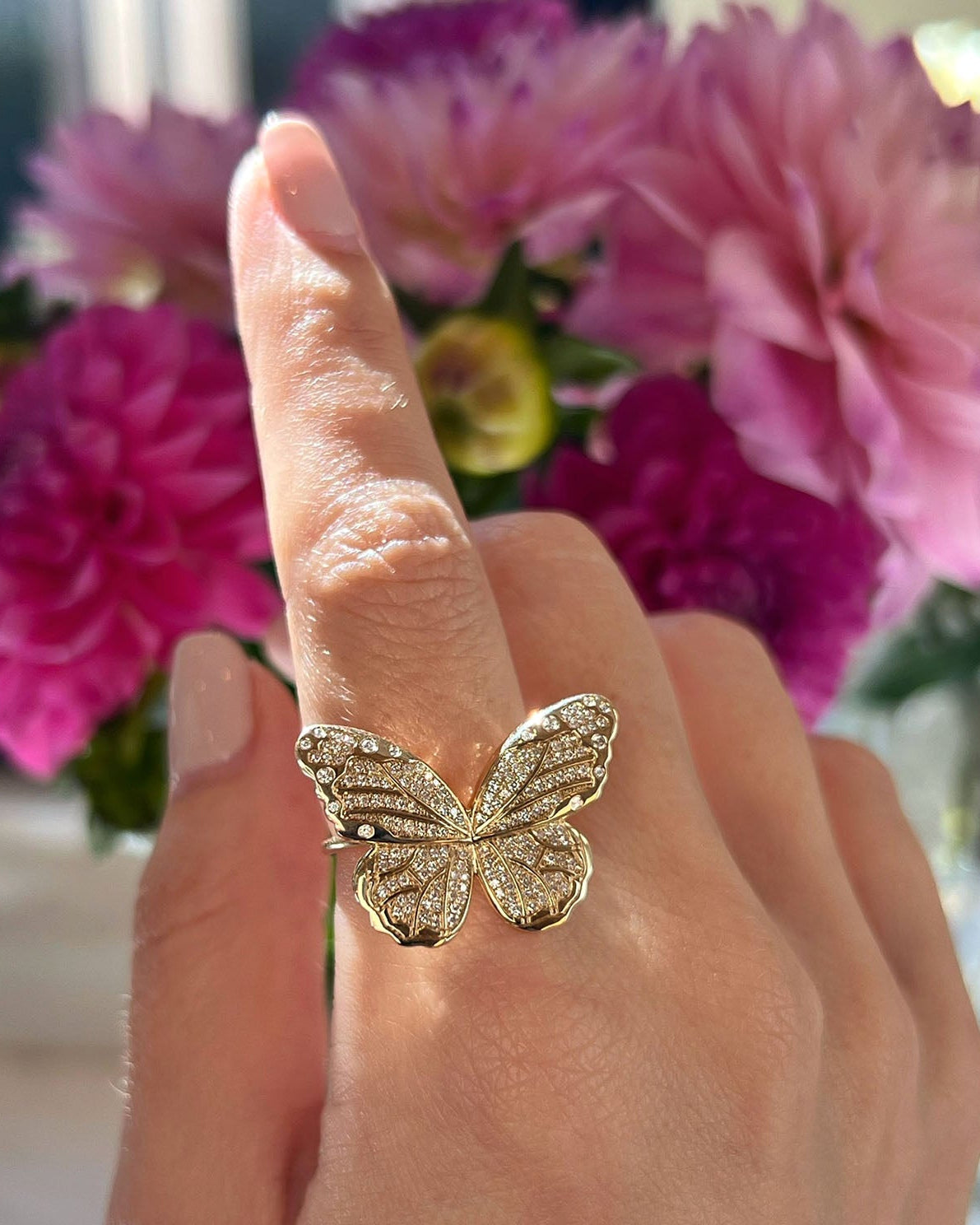 Pavé Diamond Jumbo Butterfly Ring in 14k yellow gold styled on finger of model in front of pink flowers