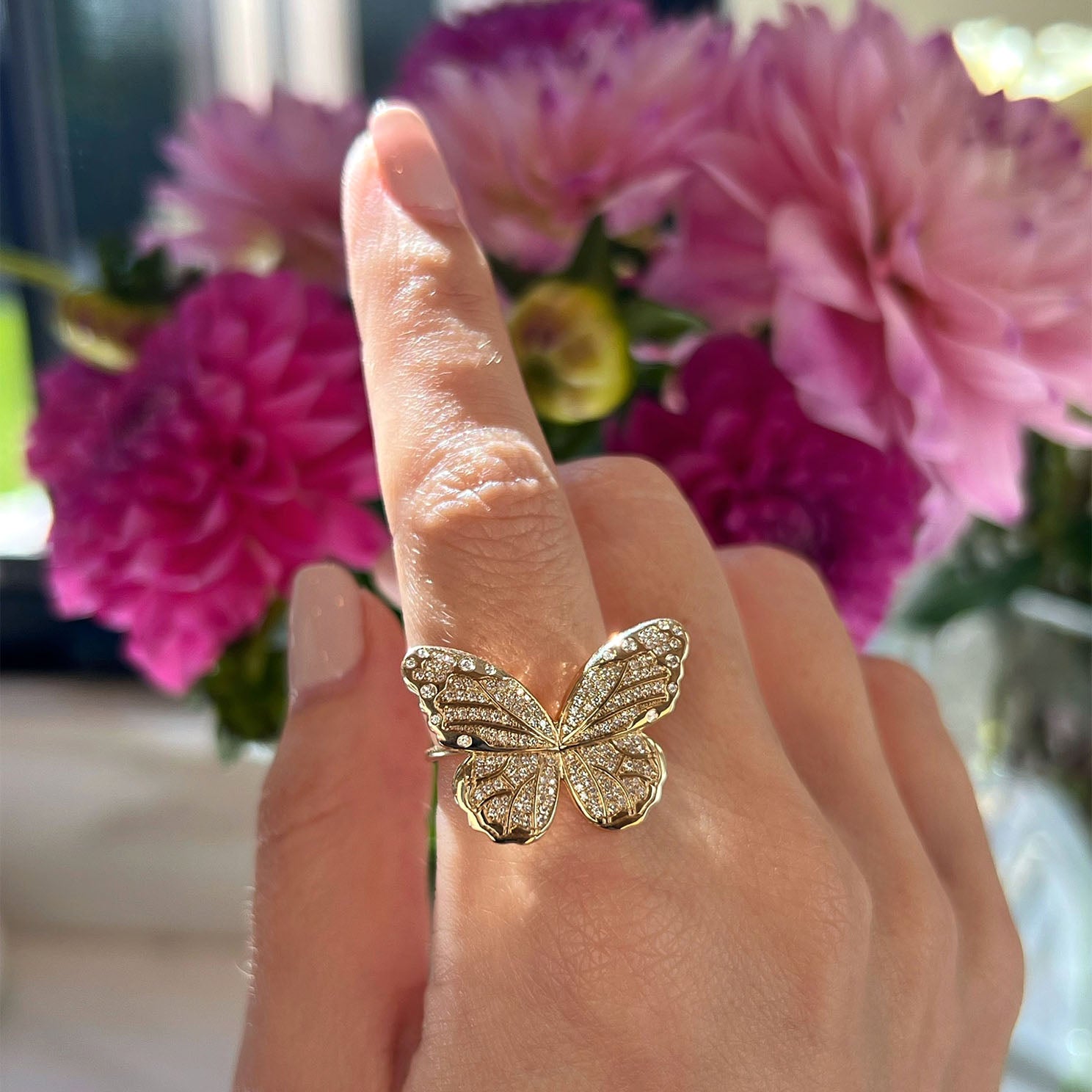 Pavé Diamond Jumbo Butterfly Ring in 14k yellow gold styled on finger of model in front of pink flowers