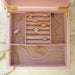 Signature Jewelry Box in the color pink displayed with 14k yellow gold rings, earrings, necklaces, and bracelets with diamonds