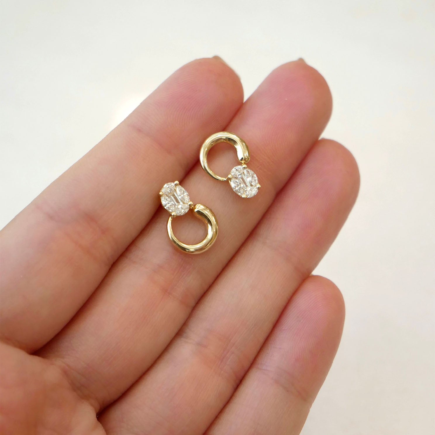 The Iris Illusion Stud Earrings in 14k yellow gold held in hand of model