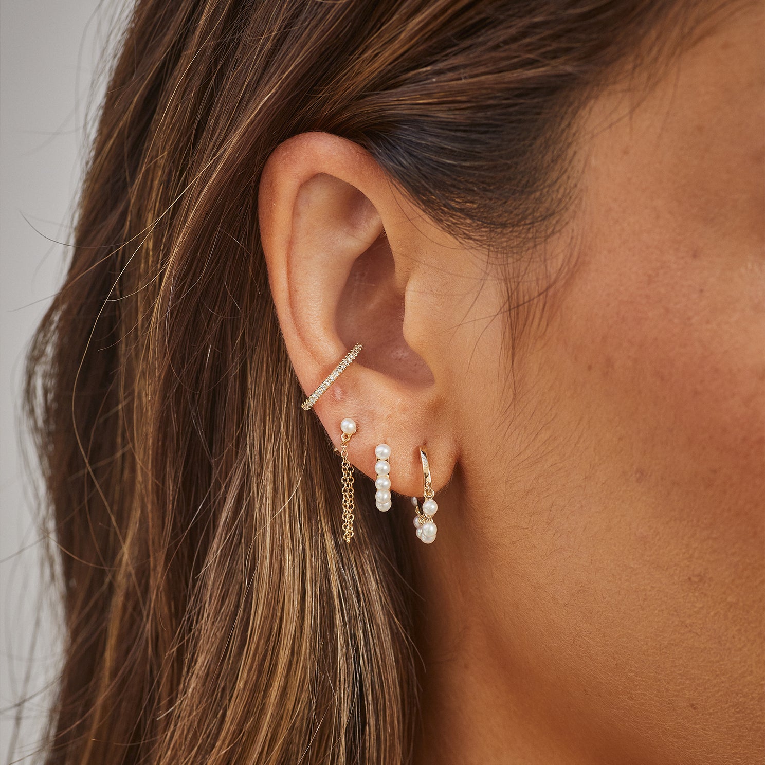 Pearl Chain Stud Earring styled on ear lobe of model with diamond, pearl, and gold earrings