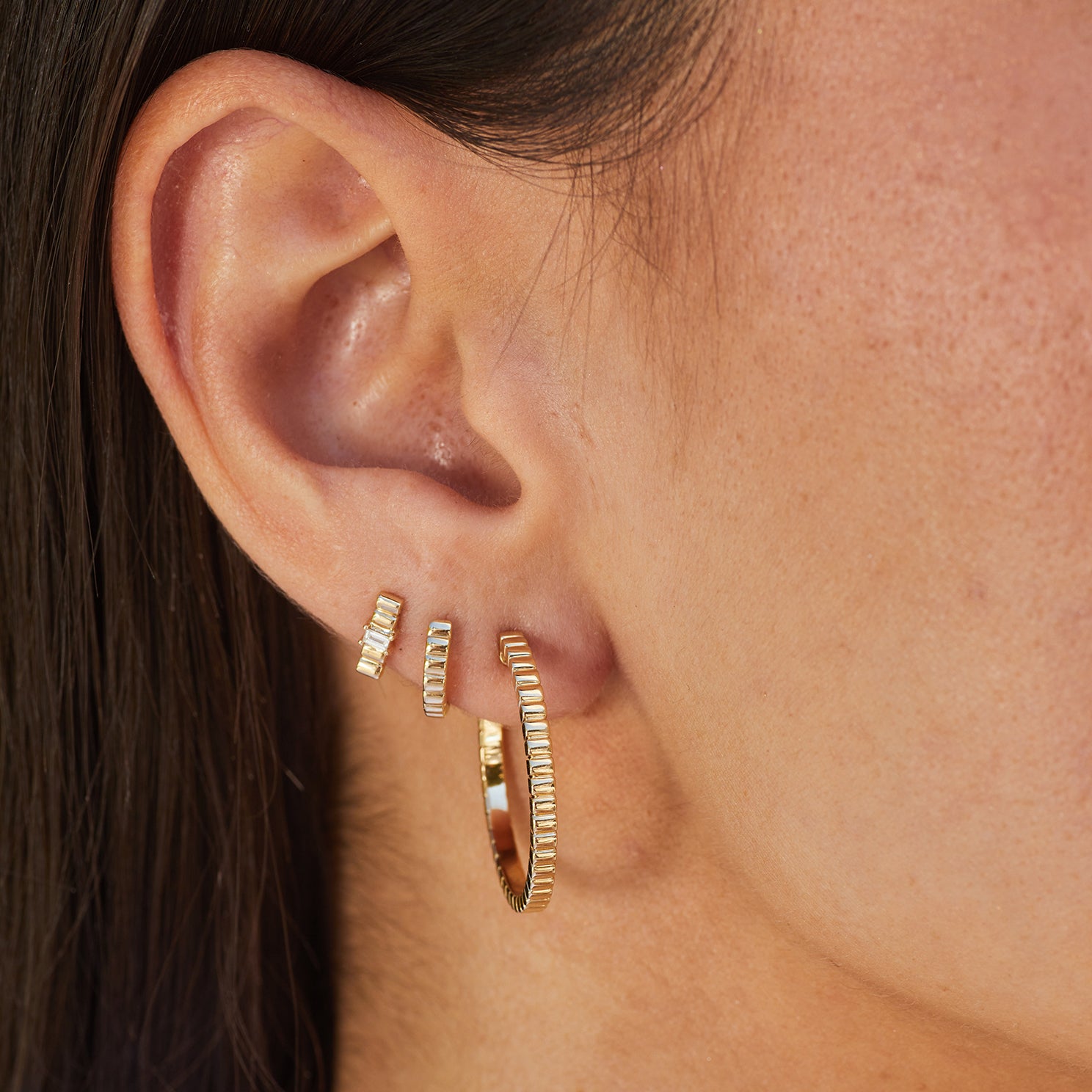 Diamond & Gold Fluted Bar Stud Earring in 14k yellow gold on third earring hole next to fluted huggie and fluted hoop earring on ear of model