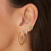 Gold Fluted Hoop Earrings in 14k yellow gold styled on first earring hole of model next to fluted huggie, prong set baguette huggie, and emerald palm tree stud on ear of model