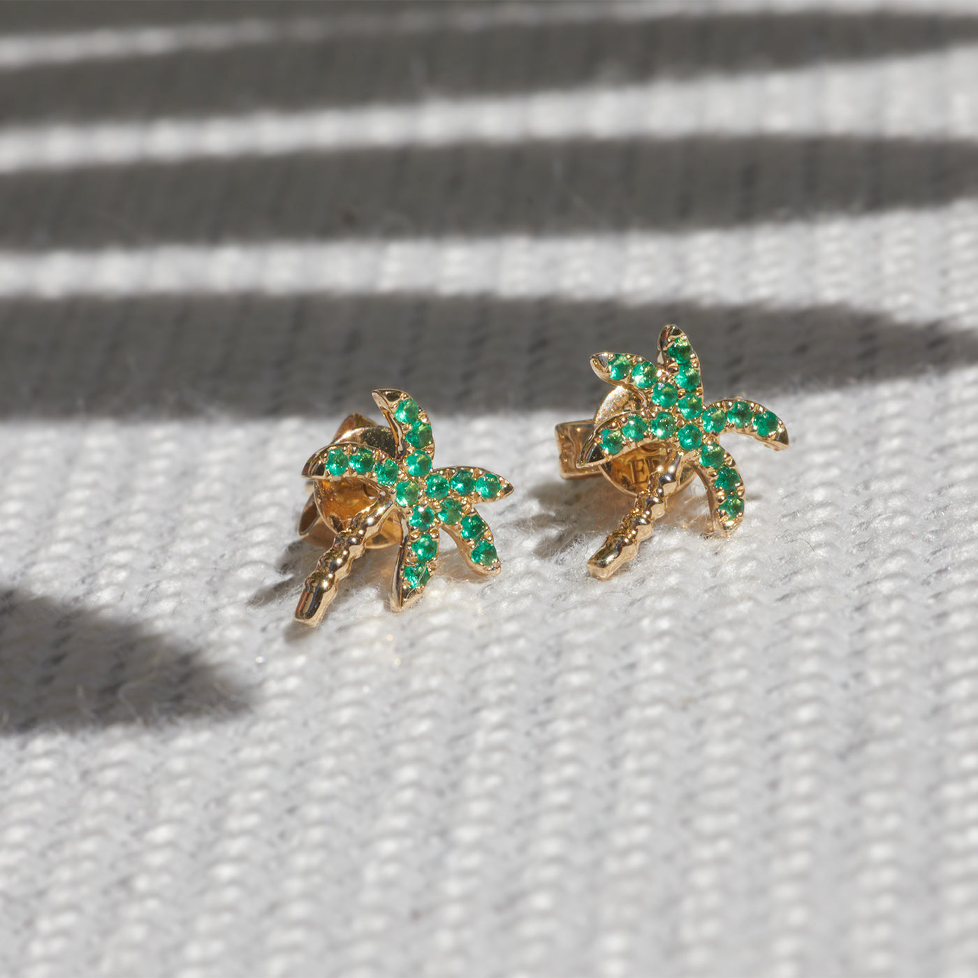 Emerald Wild Palm Stud Earring in 14k yellow gold on top of textured cloth