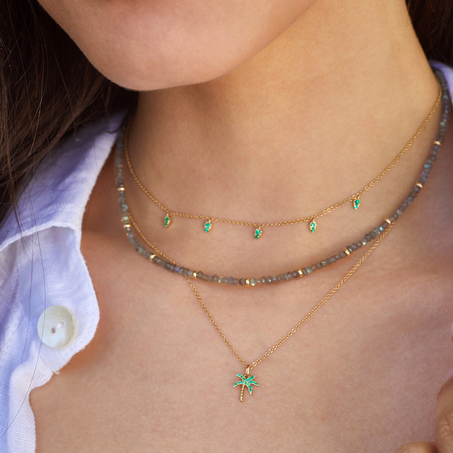 Emerald Wild Palm Necklace in 14k yellow gold styled on neck of model with emerald 5 teardrop necklace and beaded necklace