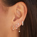 Triple Prong Set Diamond Stud Earring in 14k yellow gold featured in first and second earring hole next to diamond suspended earring and diamond jumbo huggie on ear of model