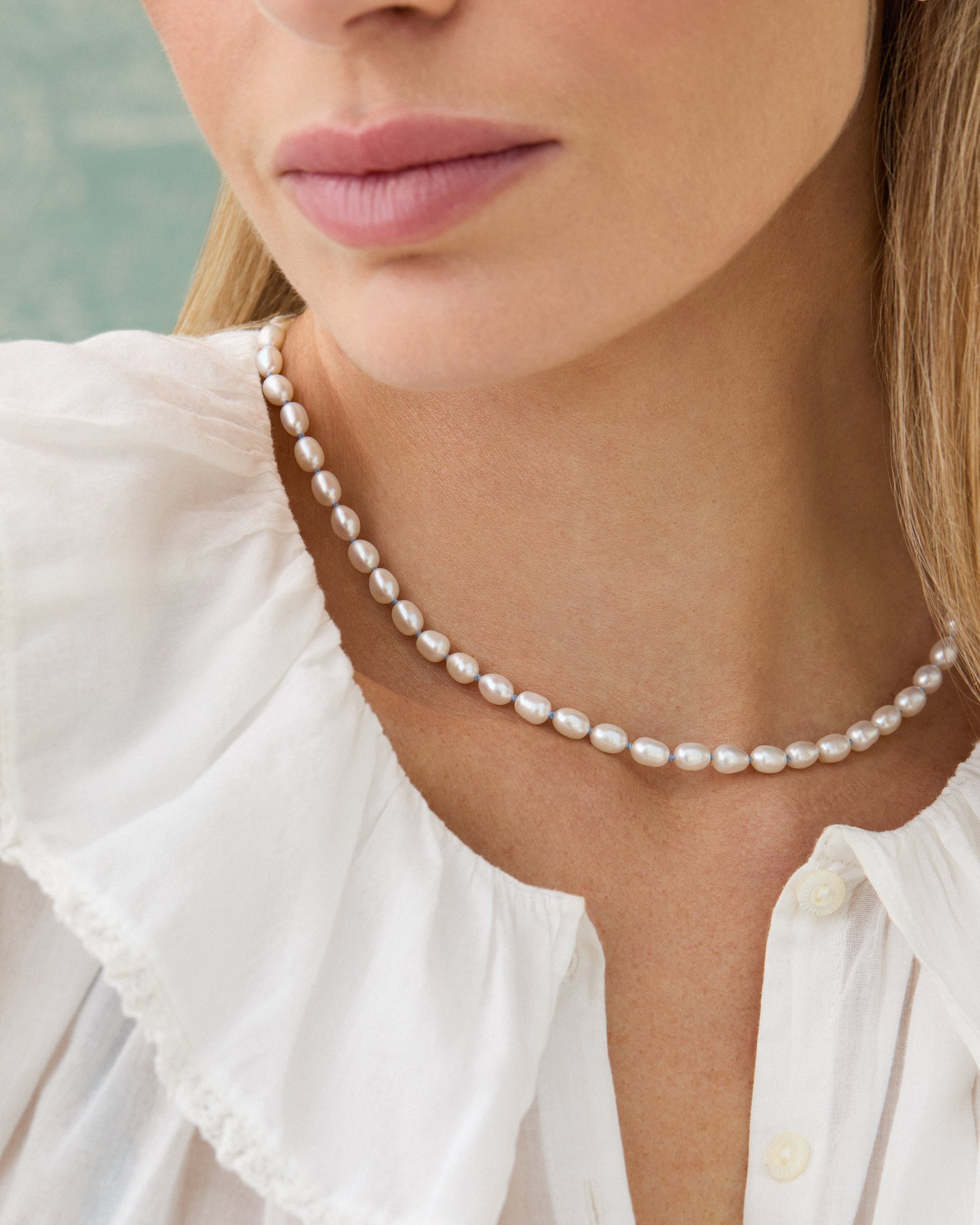 Close-up of a woman wearing a pearl necklace and earrings with a blurred background