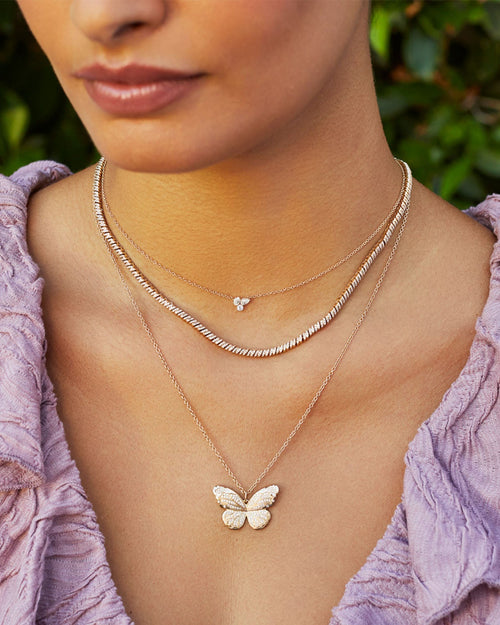 Pavé Diamond Jumbo Butterfly Necklace in 14k rose gold styled on neck of model with triple diamond cluster necklace and diamond twist necklace