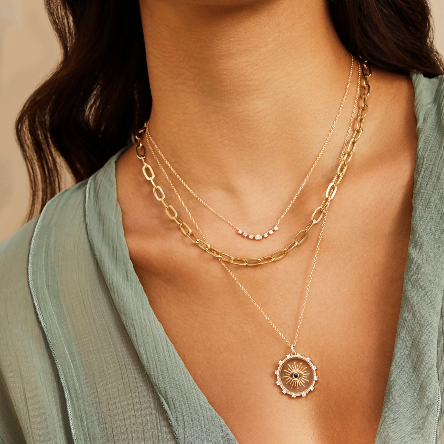 Floating Evil Eye Necklace in 14k yellow gold styled on neck of model with gold and diamond necklaces