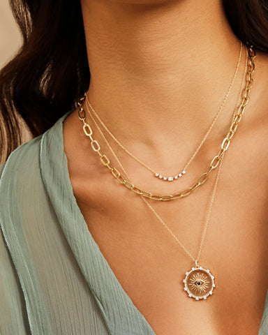 Diamond Carrie Necklace in 14k yellow gold styled on neck of model with gold and evil eye necklaces