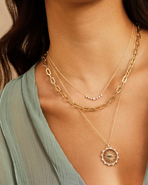 Diamond Carrie Necklace in 14k yellow gold styled on neck of model with gold and evil eye necklaces