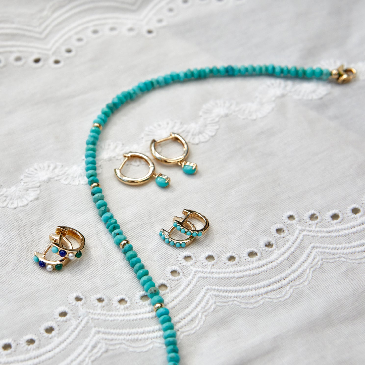 Reversible Diamond & Turquoise Mini Huggie Earring in 14k yellow gold next to gold and turquoise earrings and necklace