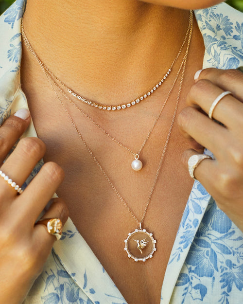 Pearl Ball Drop Necklace in 14k yellow gold styled on neck of model with diamond and hummingbird necklaces