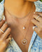 Floating Hummingbird Necklace in 14k yellow gold styled on neck of model with diamond and pearl necklaces