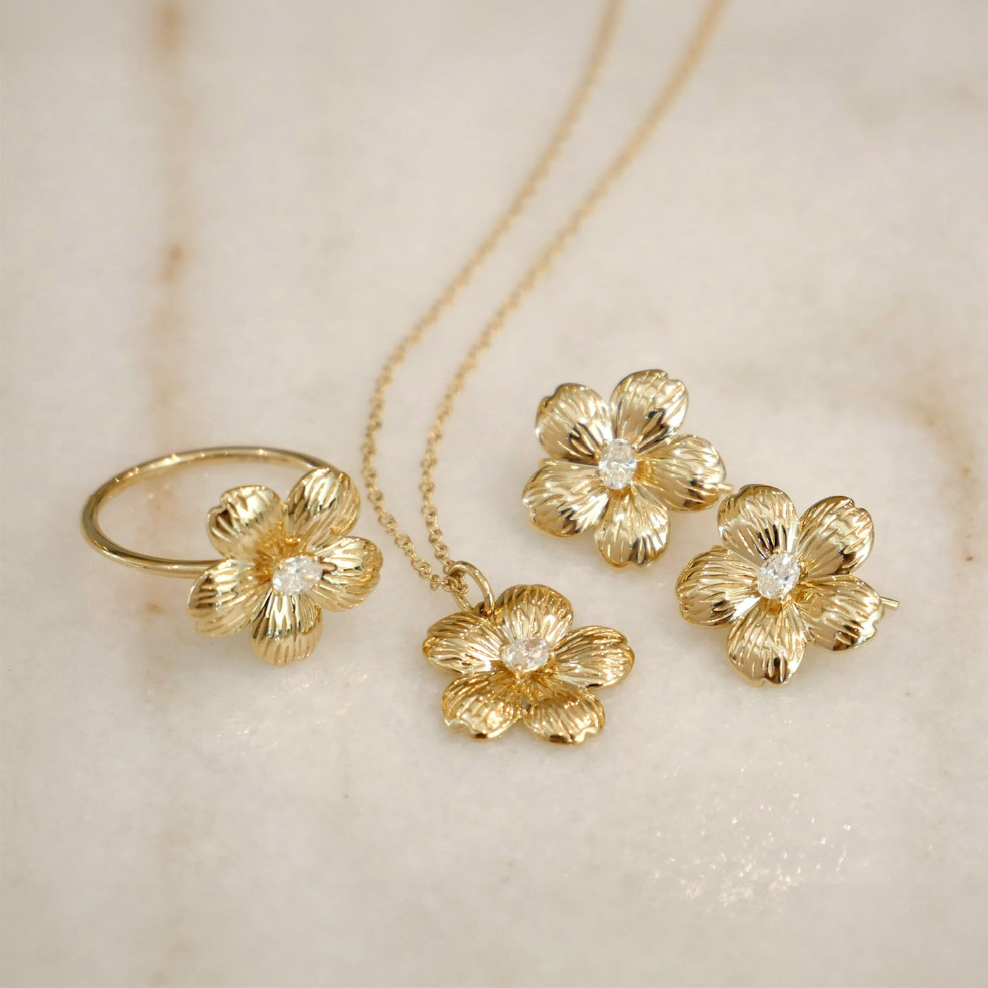 Cherry Blossom Necklace in 14k yellow gold next to Cherry Blossom Ring and Earrings