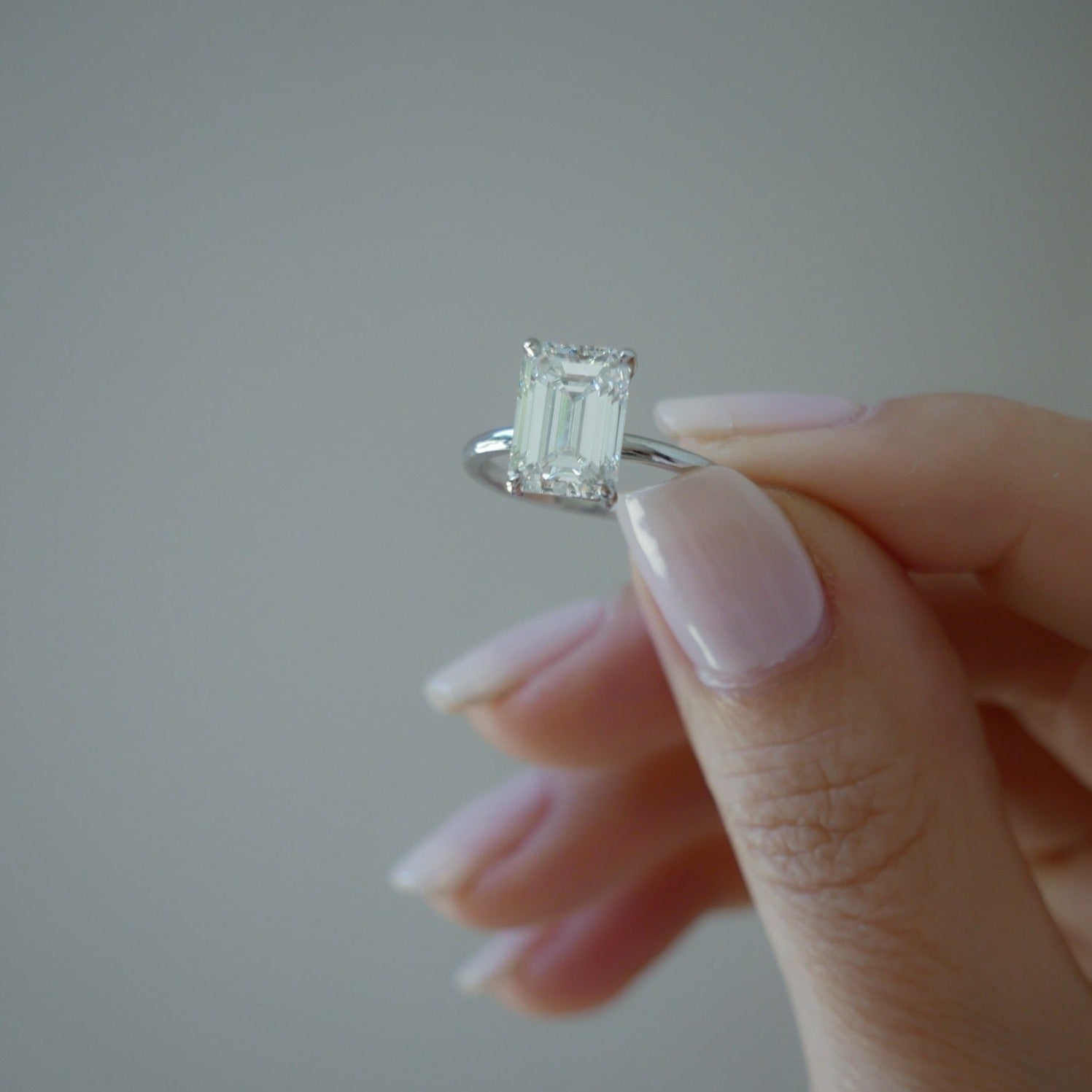 Jamie Engagement Ring with emerald cut center diamond and platinum band held in between fingers of model