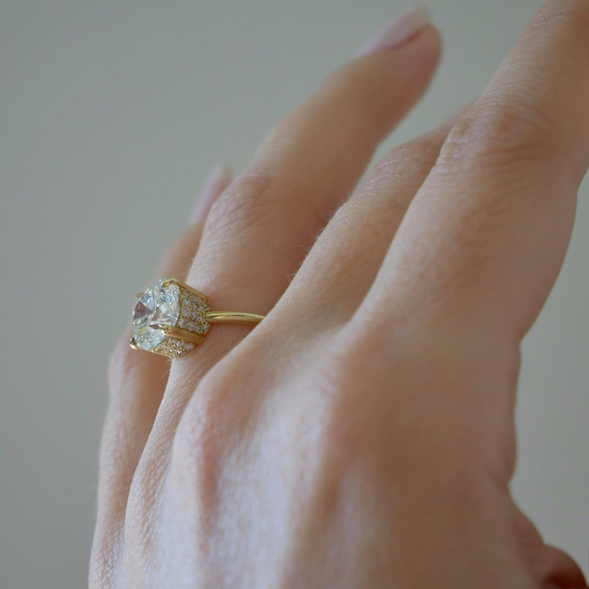 The Lindsay Engagement Ring with round center diamond, basket covered in pave diamonds, and yellow gold band styled on ring finger of model