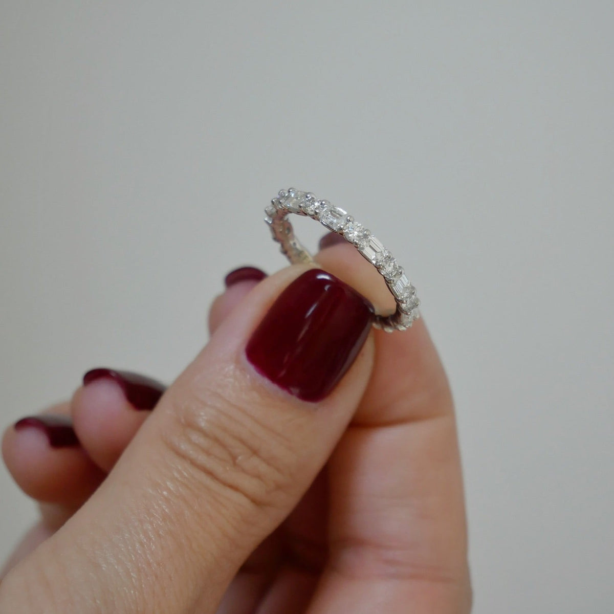 Round & Emerald Diamond Eternity Band in 18k white gold held in between fingers of model