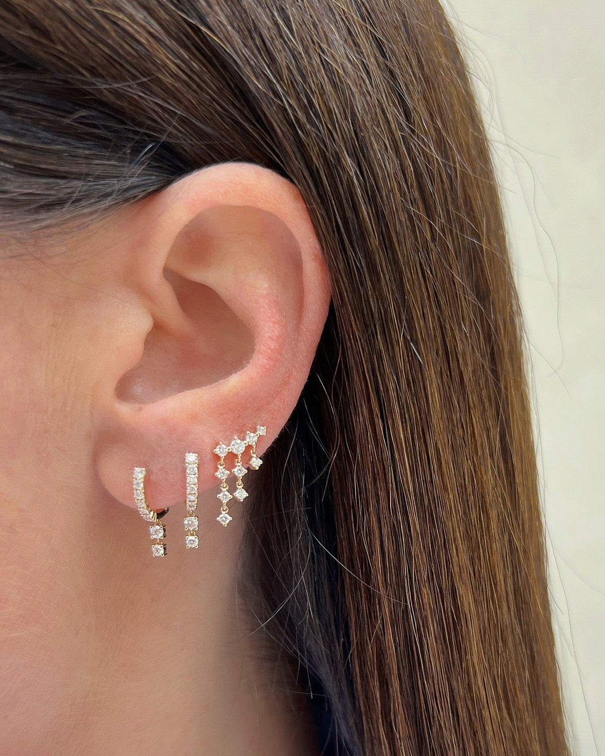 Prong Set Double Drop Huggie Earrings in 14k yellow gold styled on first and second earring hold on ear lobe of model next to diamond dangle stud earring