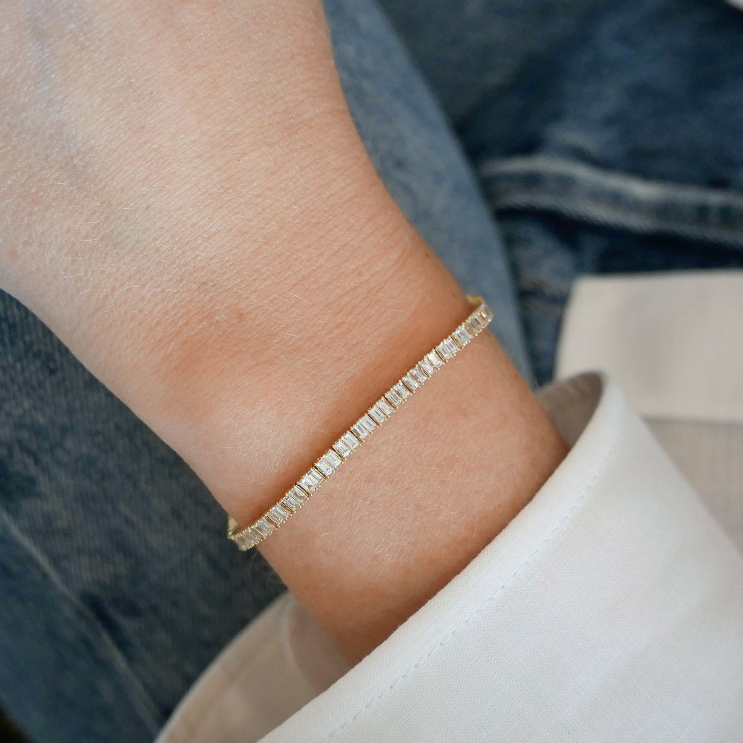 Prong Set Diamond Baguette Eternity Bracelet in 14k yellow gold styled on wrist of model with white blouse sleeve