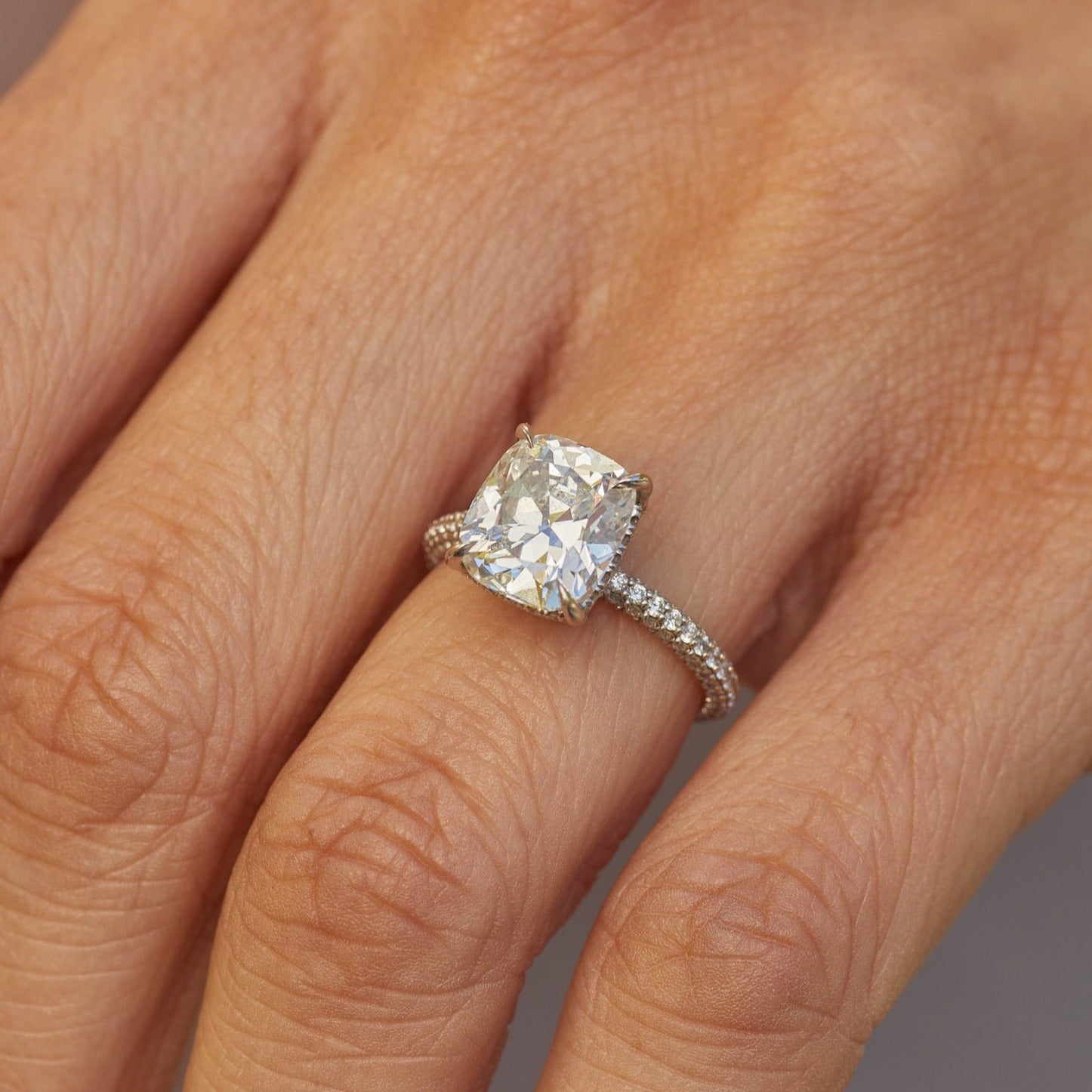 The Emily Engagement Ring with cushion cut center diamond with 3-sided micro pave diamonds on platinum band styled on ring finger of model