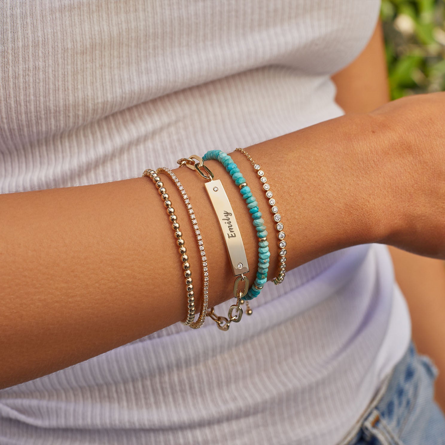 Nameplate Jumbo Link Bracelet in 14k yellow gold engraved with initials EMILY in script font styled on wrist of model with gold, diamond, and birthstone bead bracelets