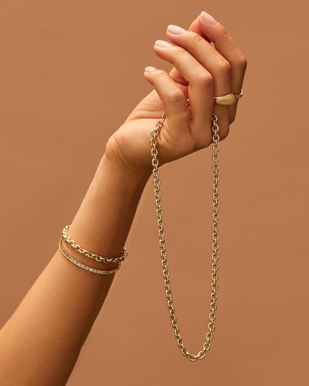 Sienna Chain Necklace in 14k yellow gold held in hand of model wearing two gold bracelets and two gold rings