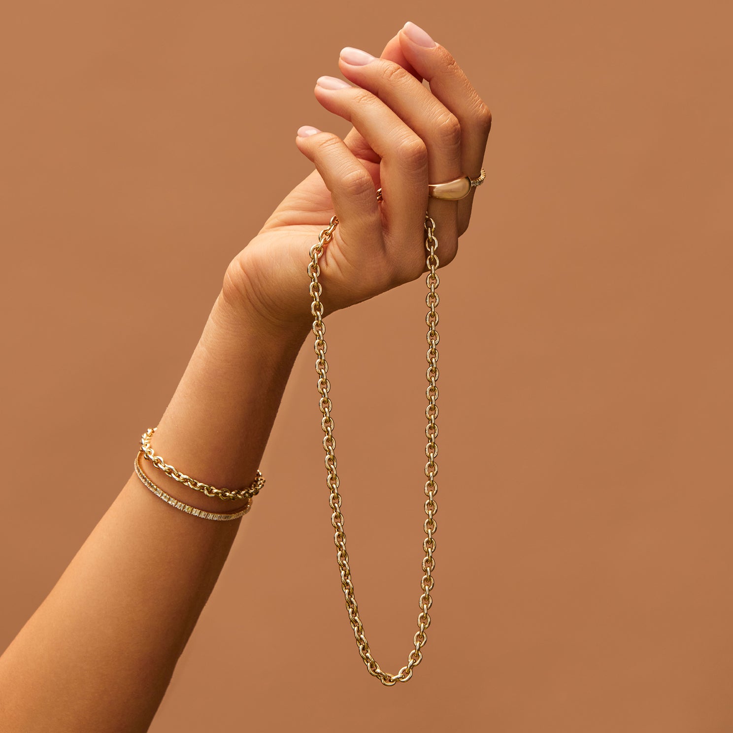 Sienna Chain Necklace in 14k yellow gold held in hand of model wearing two gold bracelets and two gold rings