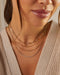 Gold and diamond necklaces styled on neck of model wearing tan sweater