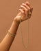 Sienna Chain Necklace in 14k yellow gold held in hand of model wearing two gold bracelets and two gold rings