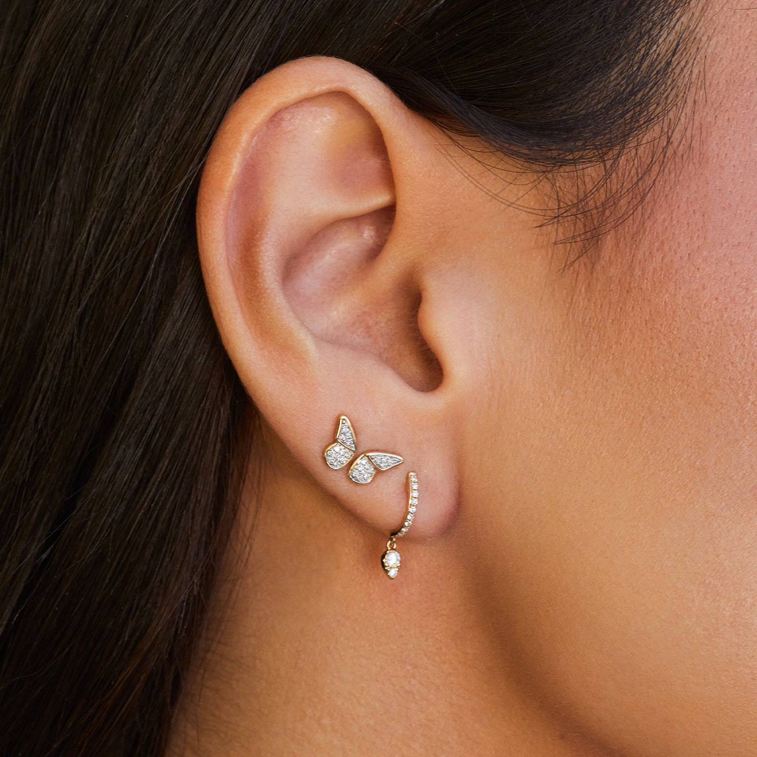 Diamond Flutter Stud Earrings in 14k yellow gold styled on second and third earring hole next to diamond huggie with teardrop on ear of model