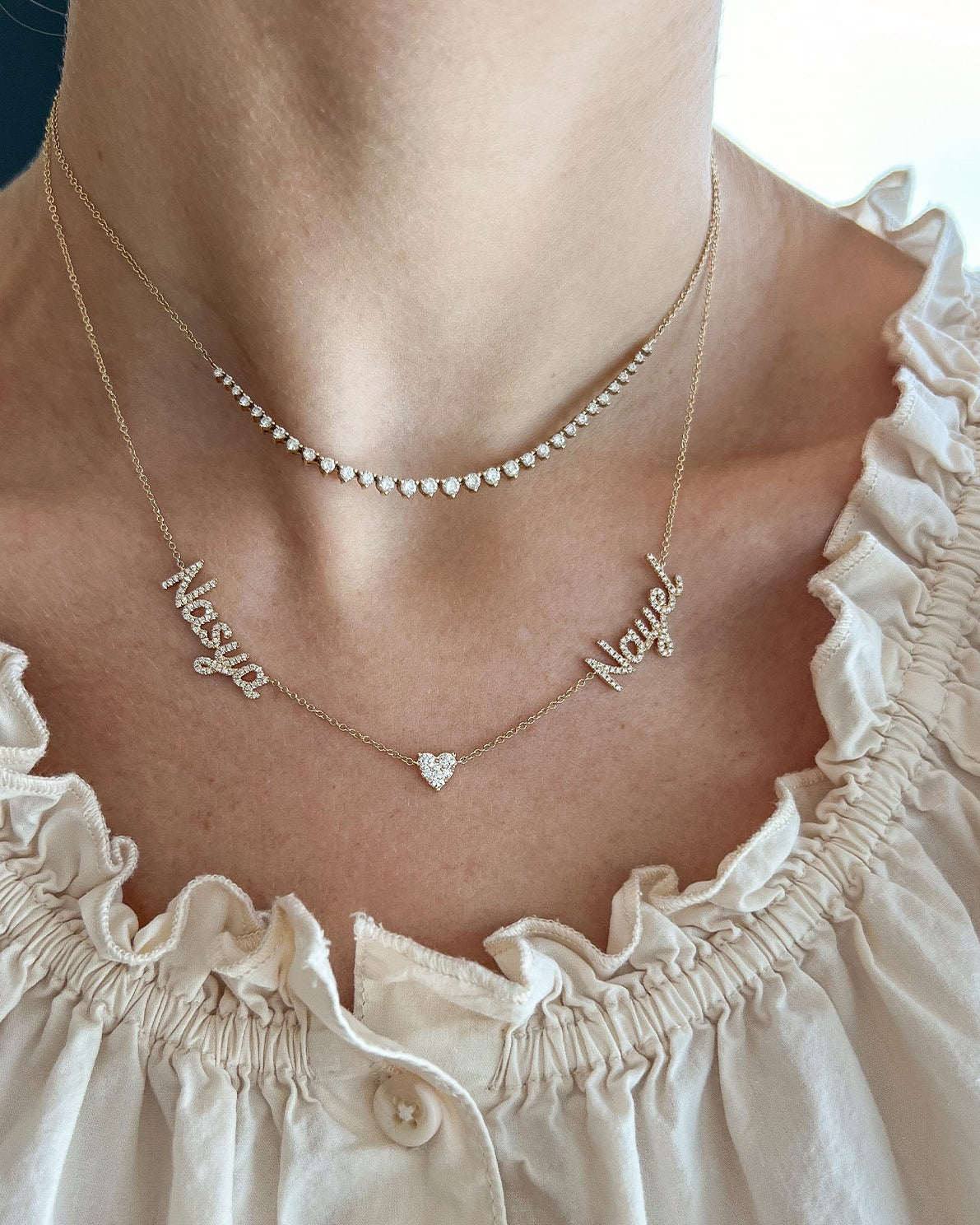 Full Cut Heart Double Diamond Script Name Necklace with names Nasya and Nayet with heart in the middle of necklace styled on neck of model with diamond segment necklace