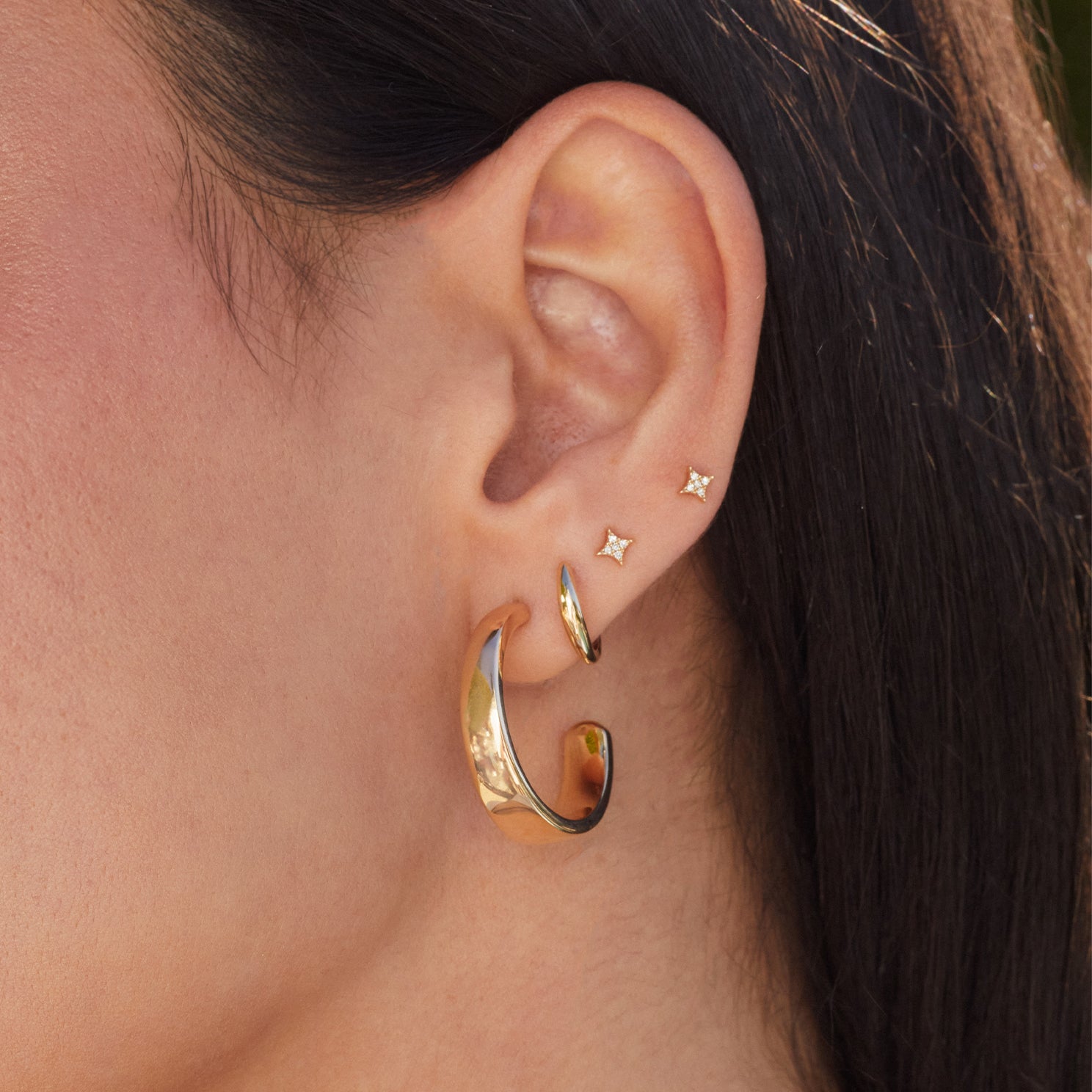 Diamond Sparkle Stud Earring in 14k yellow gold styled on third and fourth earring hole of model next to gold dome earring and gold tapered hoop earring