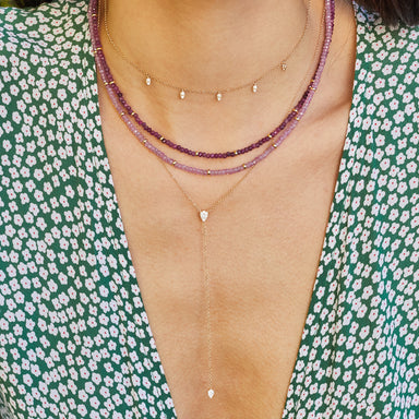 Full Cut Diamond Teardrop Lariat Necklace in 14k yellow gold styled on neck of model with gold and diamond necklace and two beaded necklaces. Model in green and white top