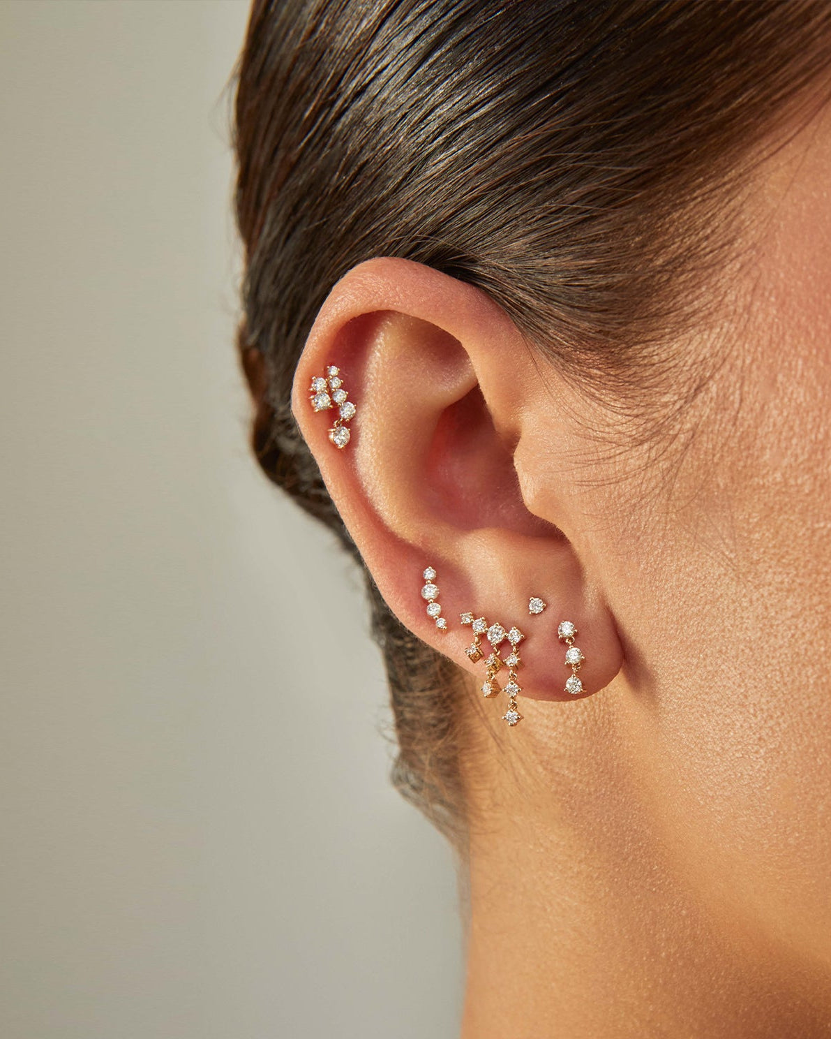 Prong Set Diamond Arc Stud Earring in 14k yellow gold styled on ear next to four diamond earrings
