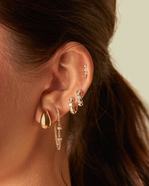 Pillow Chain Diamond Mini Huggie Earring in 14k yellow gold styled on ear with four gold and diamond earrings
