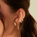 Gold Jumbo Dome Hoop Earrings in 14k yellow gold styled on first earring hole of model next to four diamond earrings