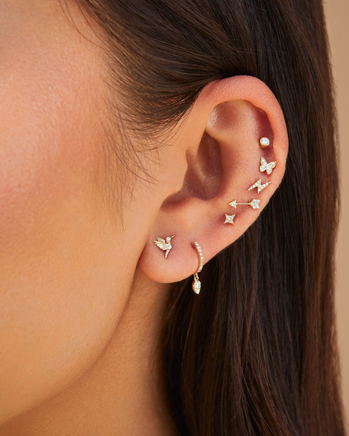Diamond Sparkle Stud Earring styled on ear lobe of model net to lightening bolt, arrow, butterfly, stud, hummingbird, and huggie earrings