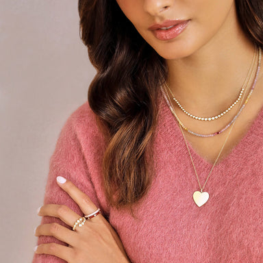 Graduated Diamond Pillow Necklace in 14k yellow gold styled on neck of model with beaded necklace and gold heart necklace