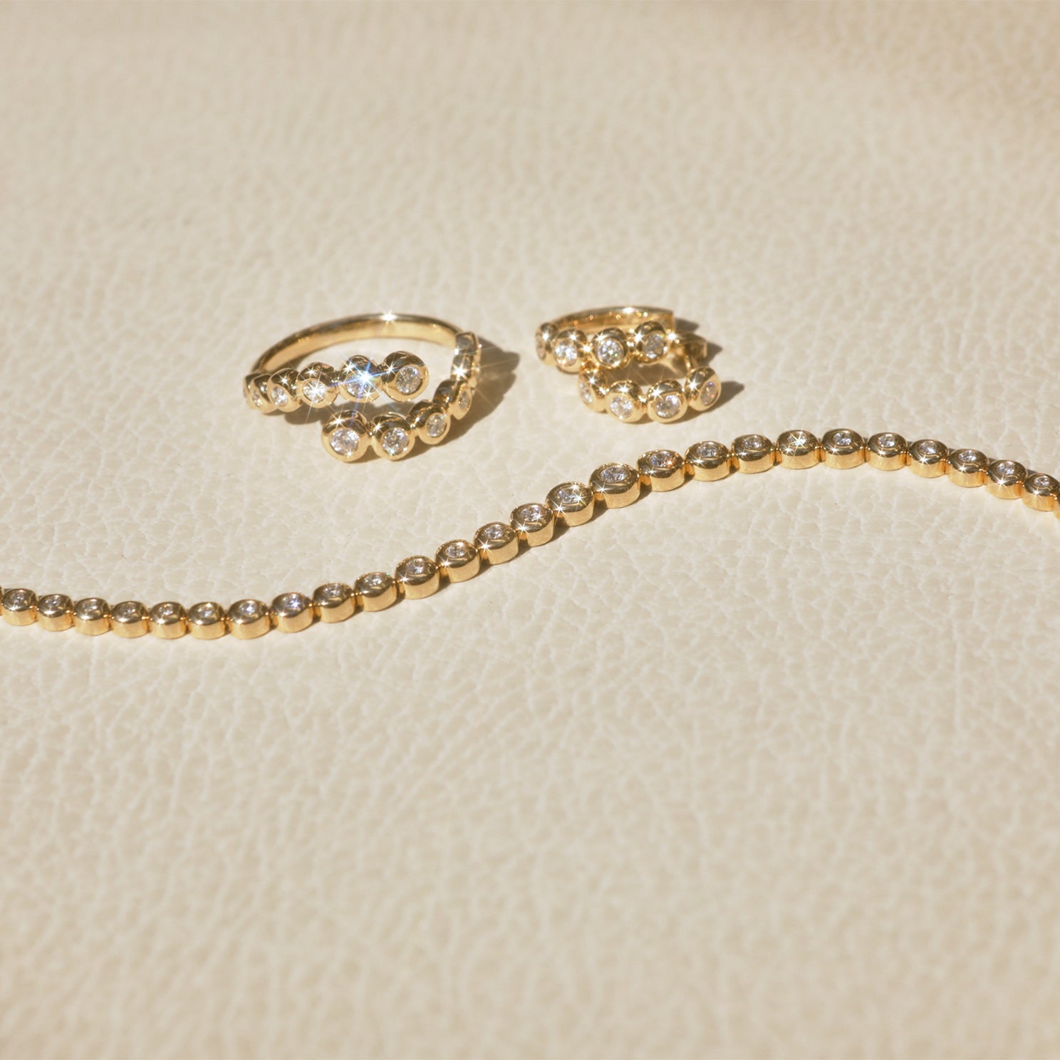 Graduated Diamond Pillow Wrap Ring in 14k yellow gold next to diamond pillow huggie earrings and diamond pillow bracelet