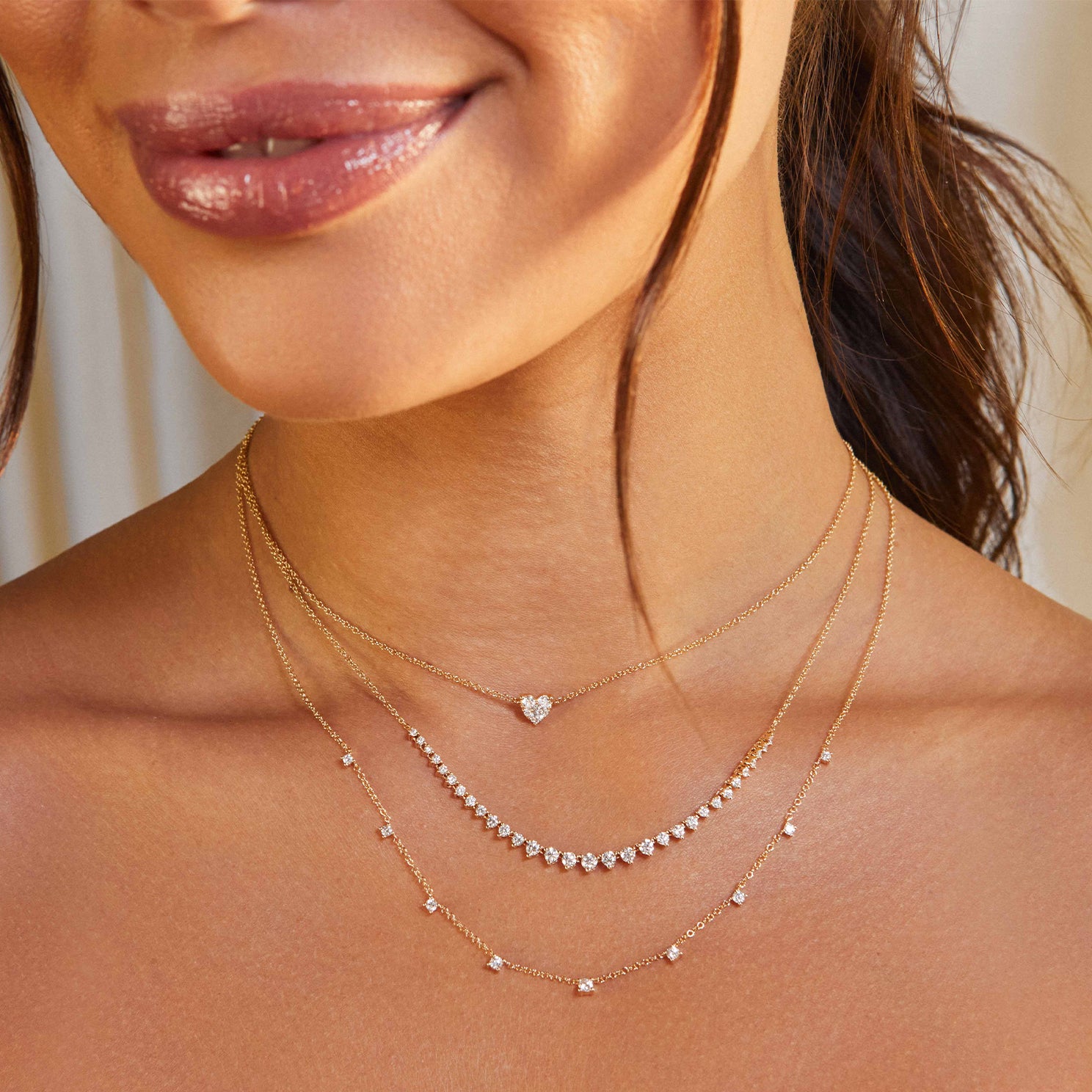 Graduated Diamond Necklace in 14k yellow gold styled on neck of model with full cut heart necklace and 9 prong diamond necklace