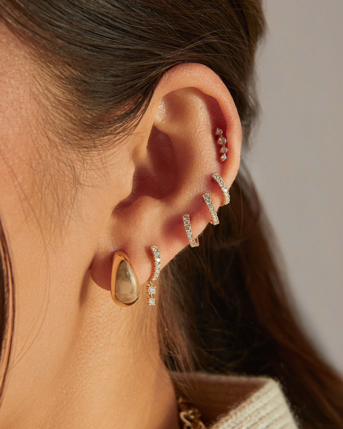 Gold Jumbo Dome Hoop Earrings in 14k yellow gold styled on first earring hole of model next to five diamond earrings