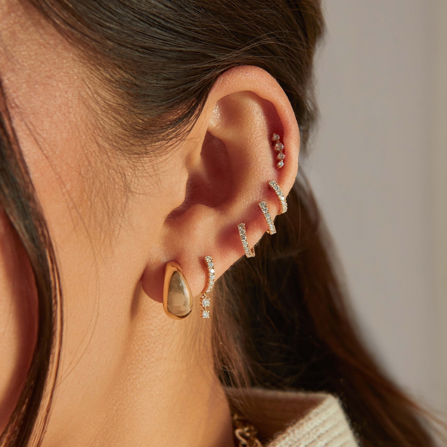 Gold Jumbo Dome Hoop Earrings in 14k yellow gold styled on first earring hole of model next to five diamond earrings