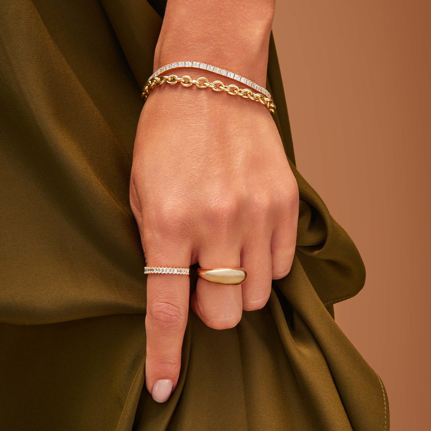 Prong Set Diamond Baguette Eternity Bracelet in 14k yellow gold styled on wrist of model next to gold chain bracelet and two rings styled on fingers
