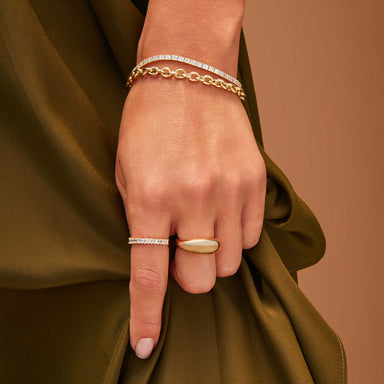 Gold Jumbo Dome Ring in 14k yellow gold styled on middle finger of model next to diamond baguette ring and diamond and gold bracelets styled on wrist of model