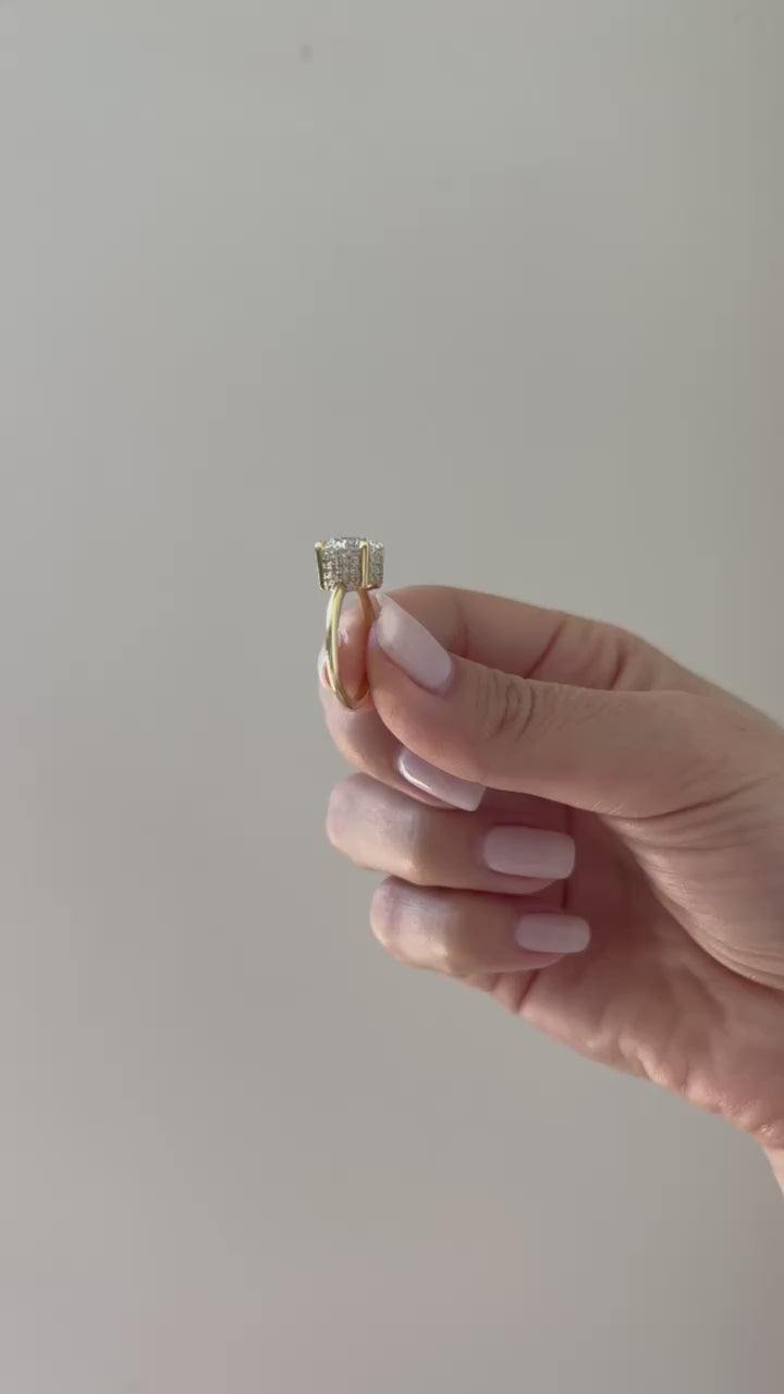 The Lindsay Engagement Ring with round center diamond, basket covered in pave diamonds, and yellow gold band held in between fingers of model and put on ring finger with no audio