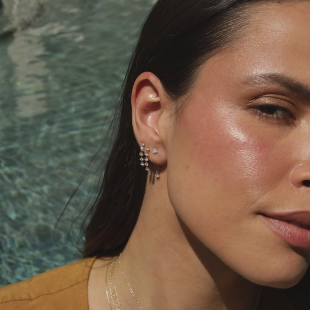 Suspended Diamond Stud Earring in 14k yellow gold on first earring hole of model next to diamond multi chain stud earrings on model tucking hair back with no audio