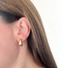 Gold Star of David Earring in 14k yellow gold styled on ear lobe of model next to jumbo hoop earring